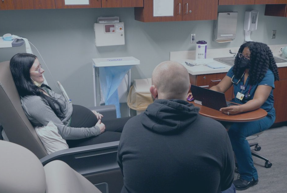 OB provider sitting in exam room with pregnant patient and their partner.