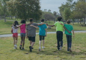 Kids walking arm in arm outdoors away from the camera.