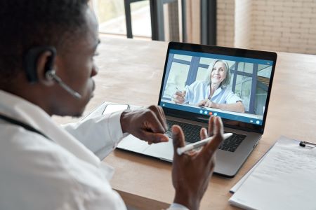 Black male sitting in front of a laptop mid-conversation with a white woman on a video call.