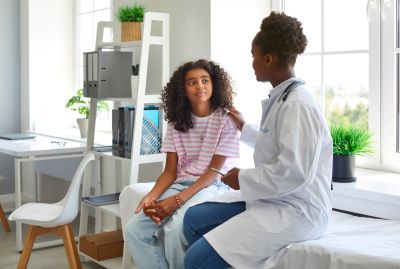 Black female doctor sits next to her black teen patient to offer comfort in the treatment room.
