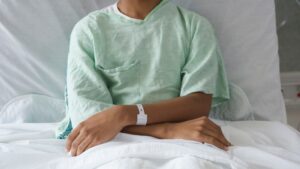 Adolescent patient sits in a hospital gown on a hospital bed.