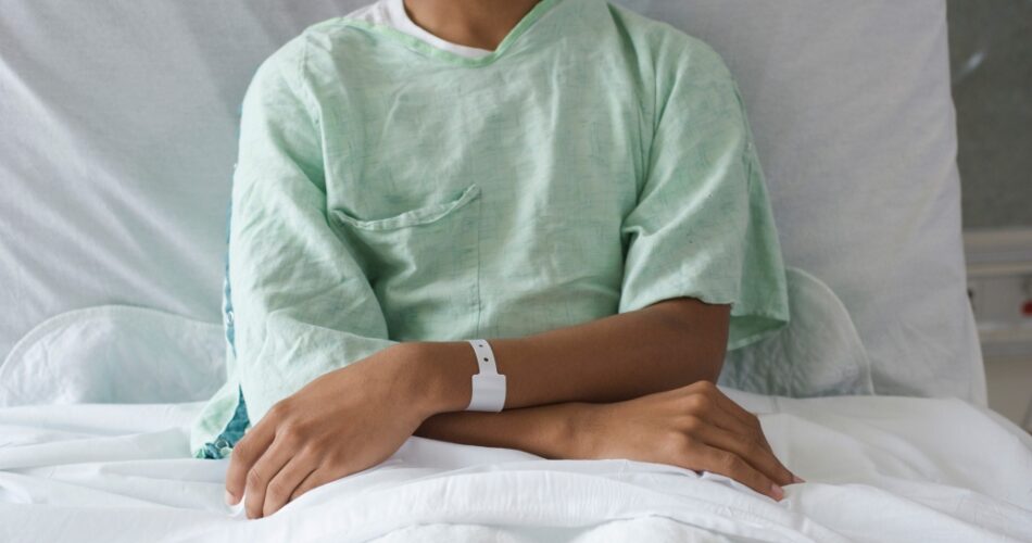 Adolescent patient sits in a hospital gown on a hospital bed.