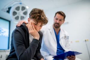 A doctor sits next to a young distressed patient in a treatment room.