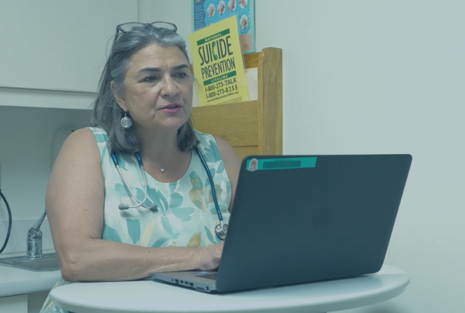 A doctor stands at her laptop in a treatment room.