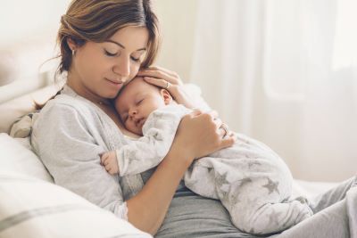 A mother cuddles with her baby in bed.