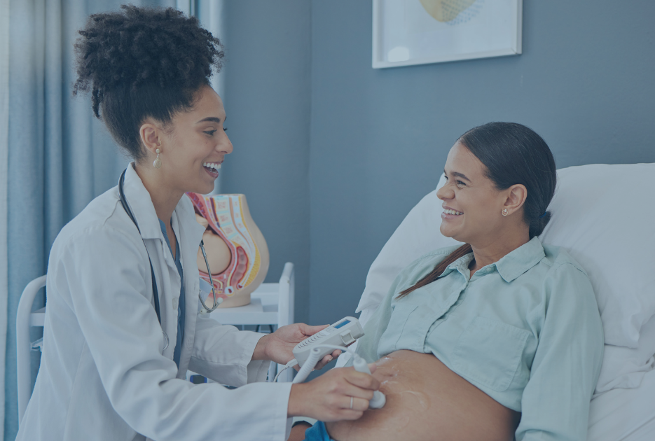 A doctor listens to a pregnant patient's heart beat in a treatment room.