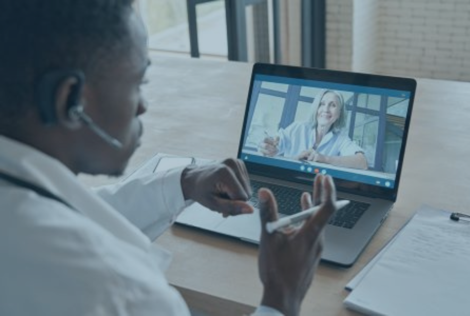 A physician sits at a desk looking at a laptop during a virtual meeting.