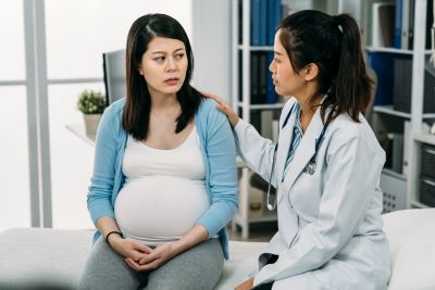 Doctor comforting and sitting next to a pregnant patient in her office.