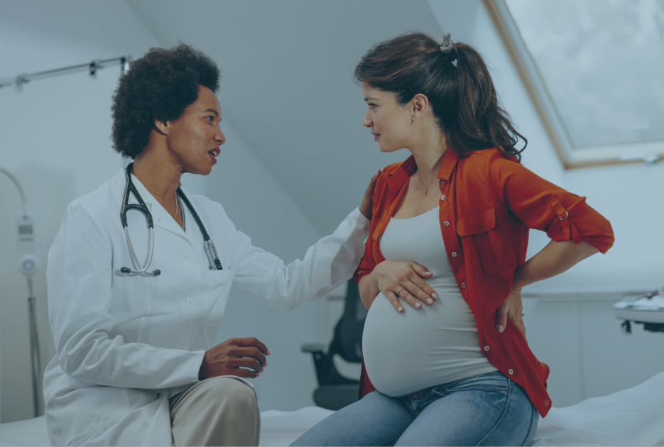 A doctor sits next to a pregnant patient and comforts her.