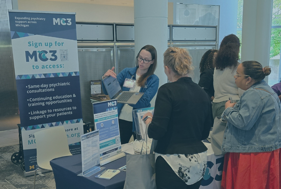 MC3 team member shows a group of people at an event how to navigate the MC3 website on a laptop.