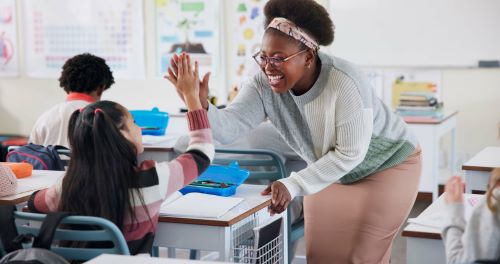 Teacher high fives a student in classroom.